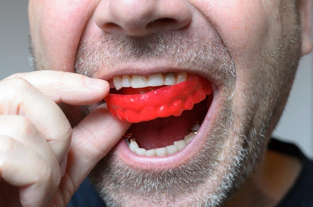 Man inserting a red mouth guard into his mouth
