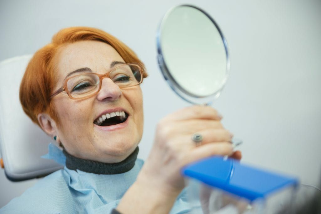 Senior woman looking at her smile in the mirror