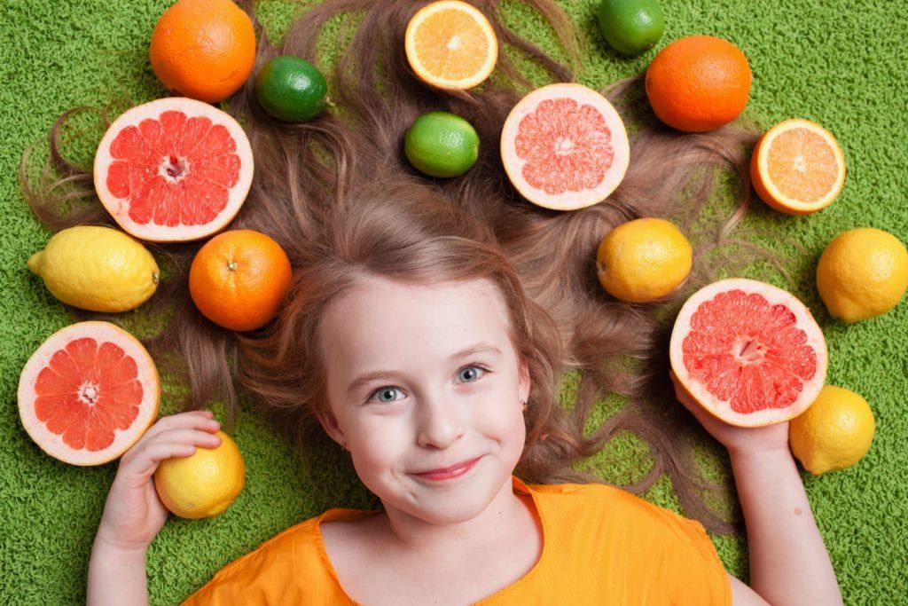 young girl laying with citrus fruits strewn about around her